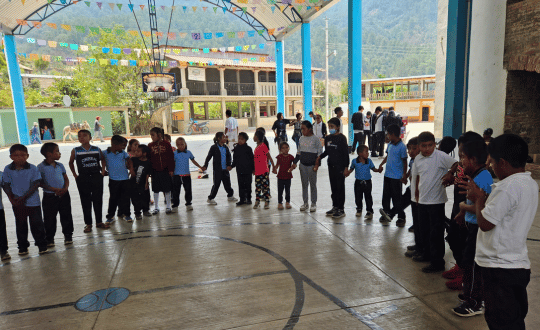 Niños y niñas participando en una dinámica comunitaria de educación popular en una cancha techada en la Sierra Sur.